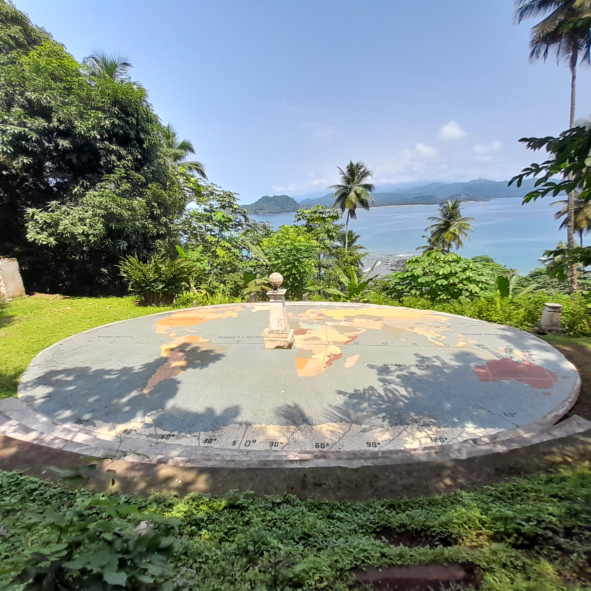 Runder Globus im Garten mit tropischen Palmen, Blick auf Meer und Berge bei klarem Himmel.